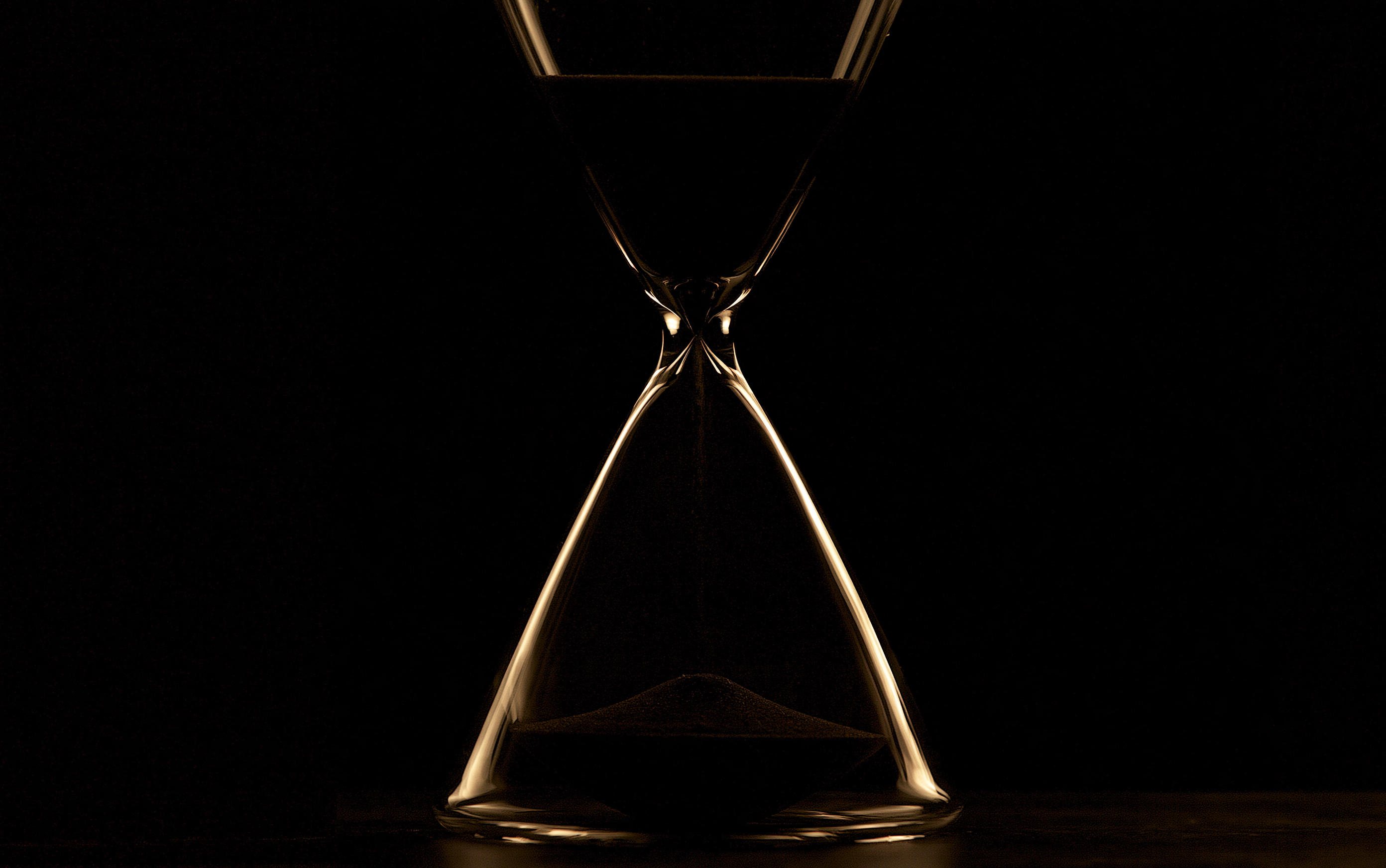 An hourglass in darkness, its glass edges traced by warm light